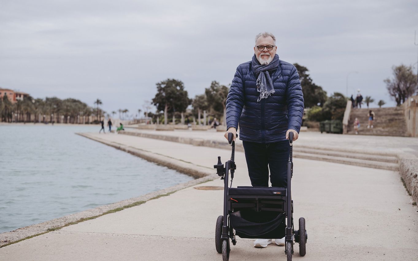 En ældre mand går med en rollator langs en havnekant