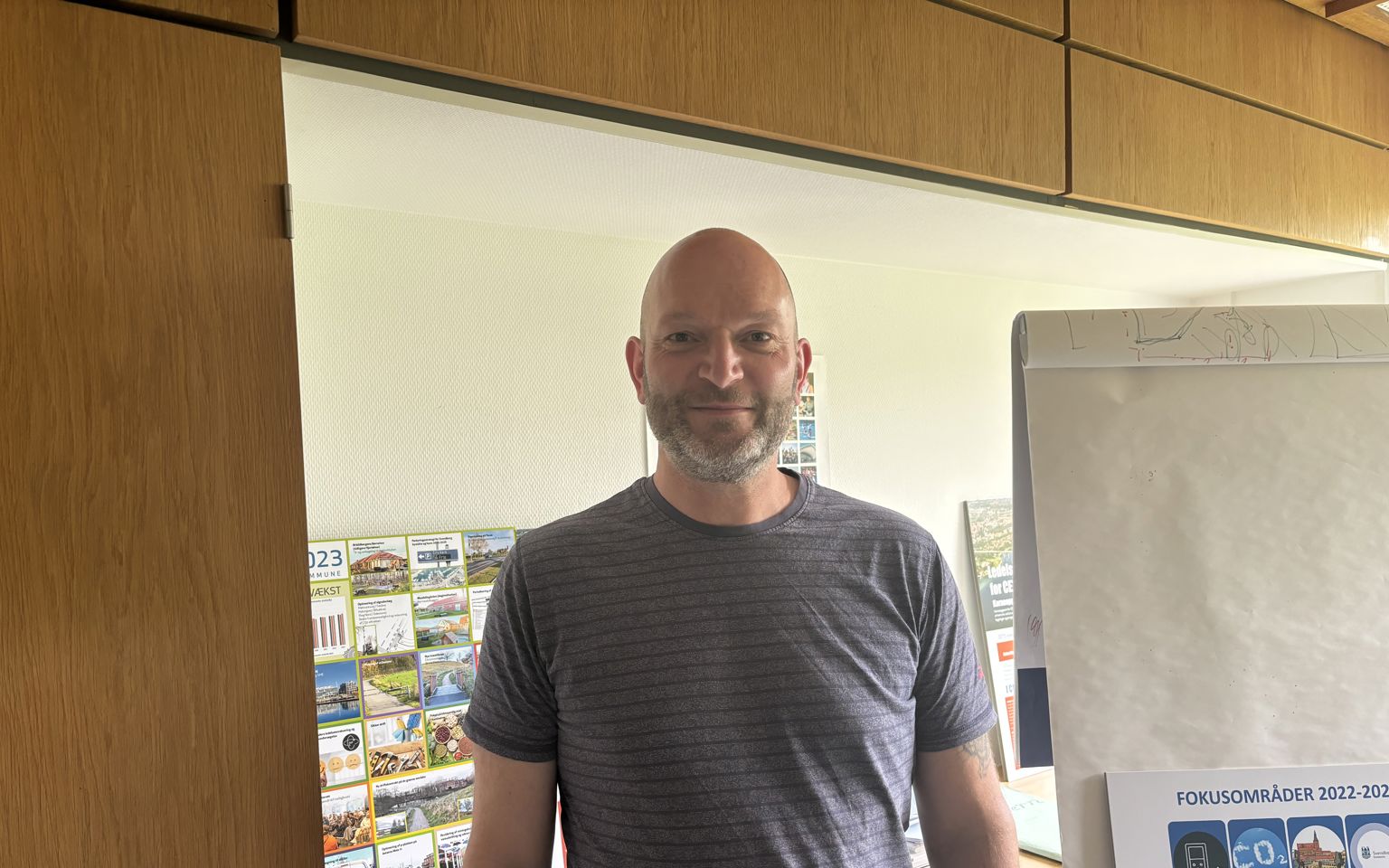 Midaldrende mand med skæg, som står foran brochurer og flipover