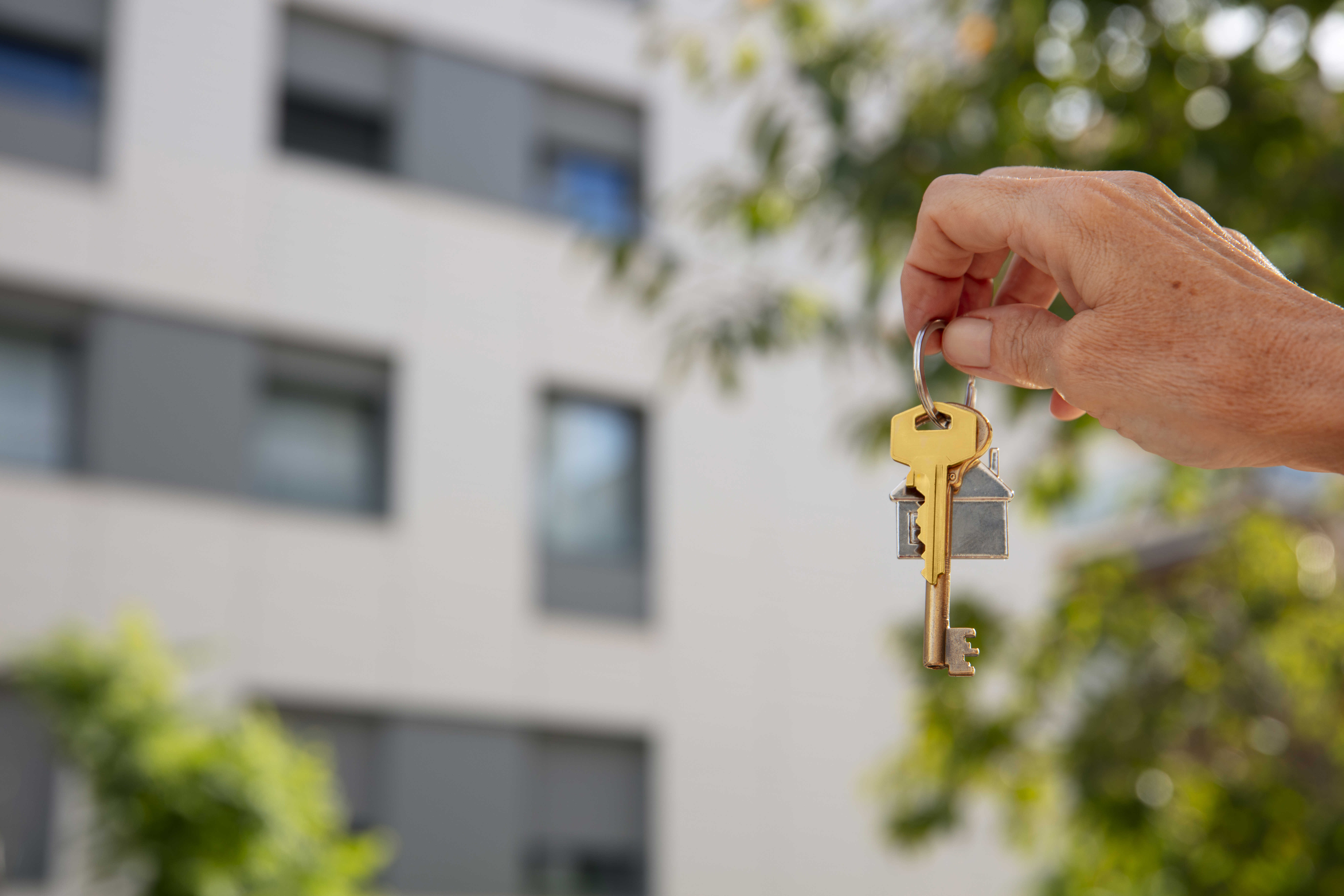 Hånd holder husnøgler. Et hus ses sløret i baggrunden