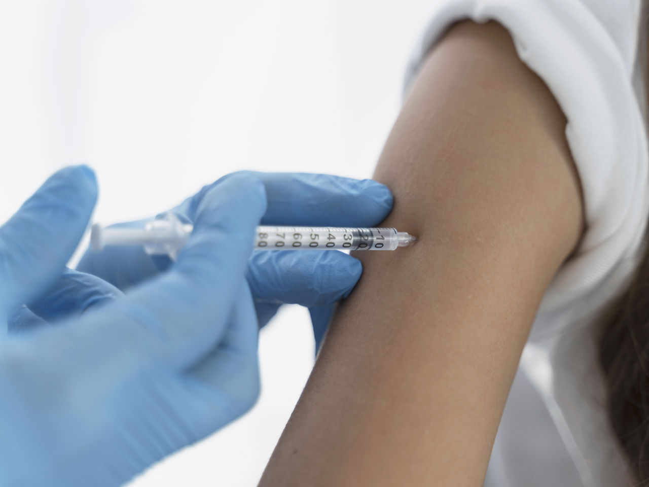 En handskebeklædt hånd vaccinerer en blottet overarm