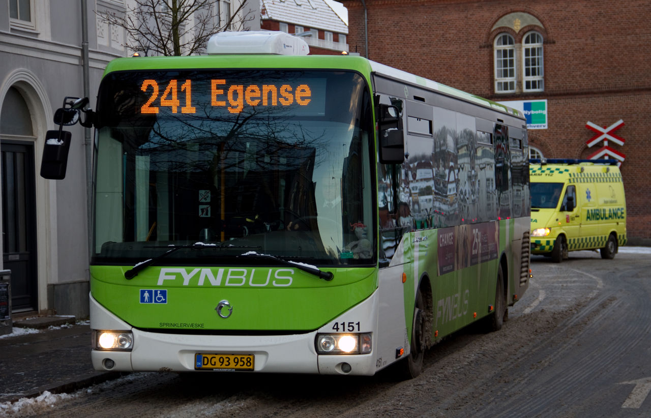 En grøn og hvis bus med 'Egense' som destination kører på en vej i byen.