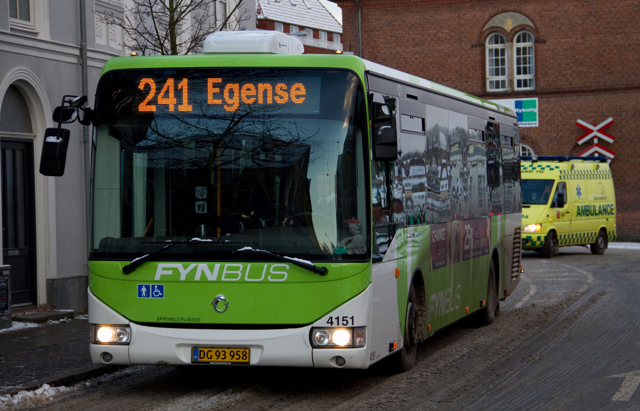 En grøn og hvis bus med 'Egense' som destination kører på en vej i byen.