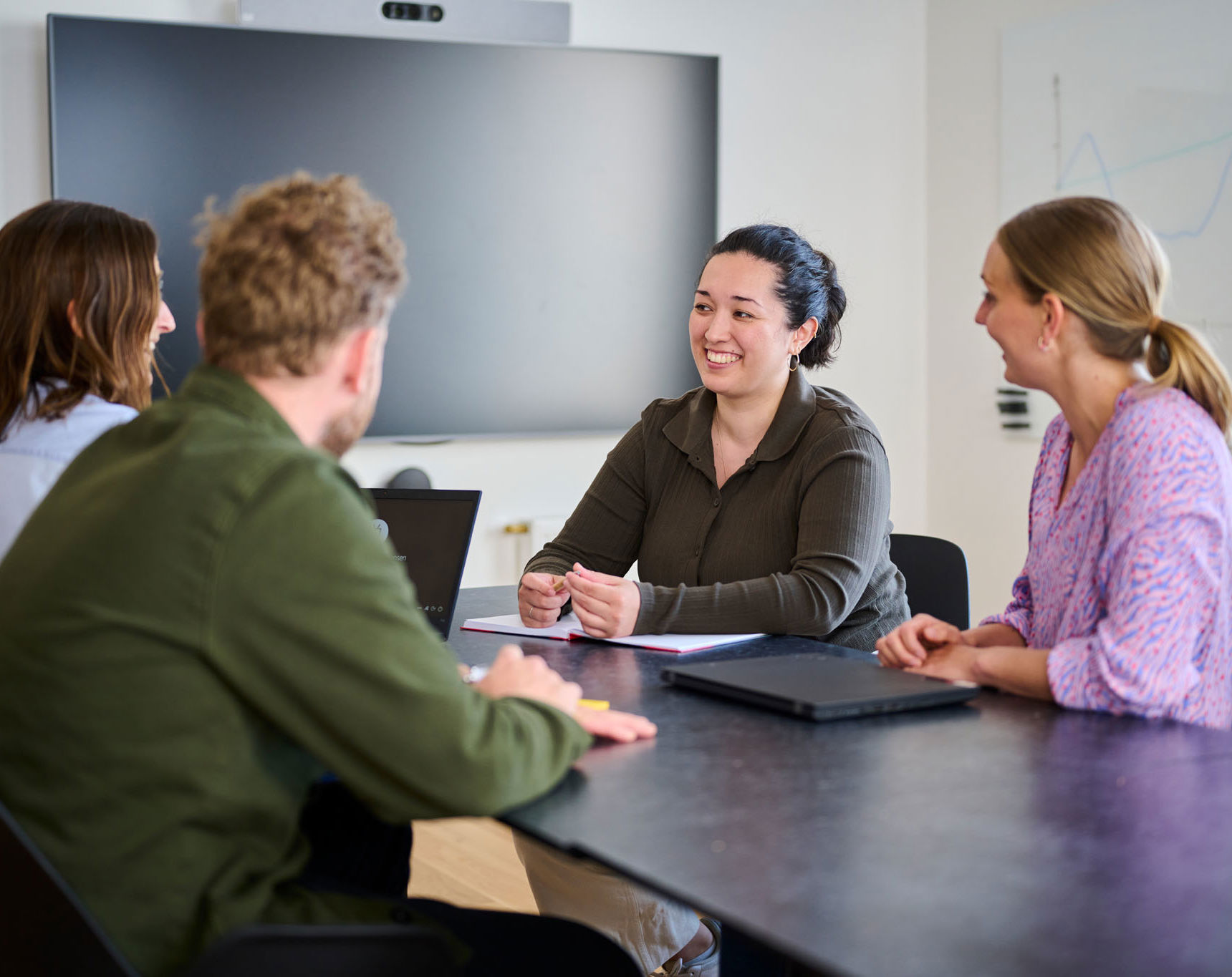 Tre kvinder og en mand sidder rundt om bord og snakker