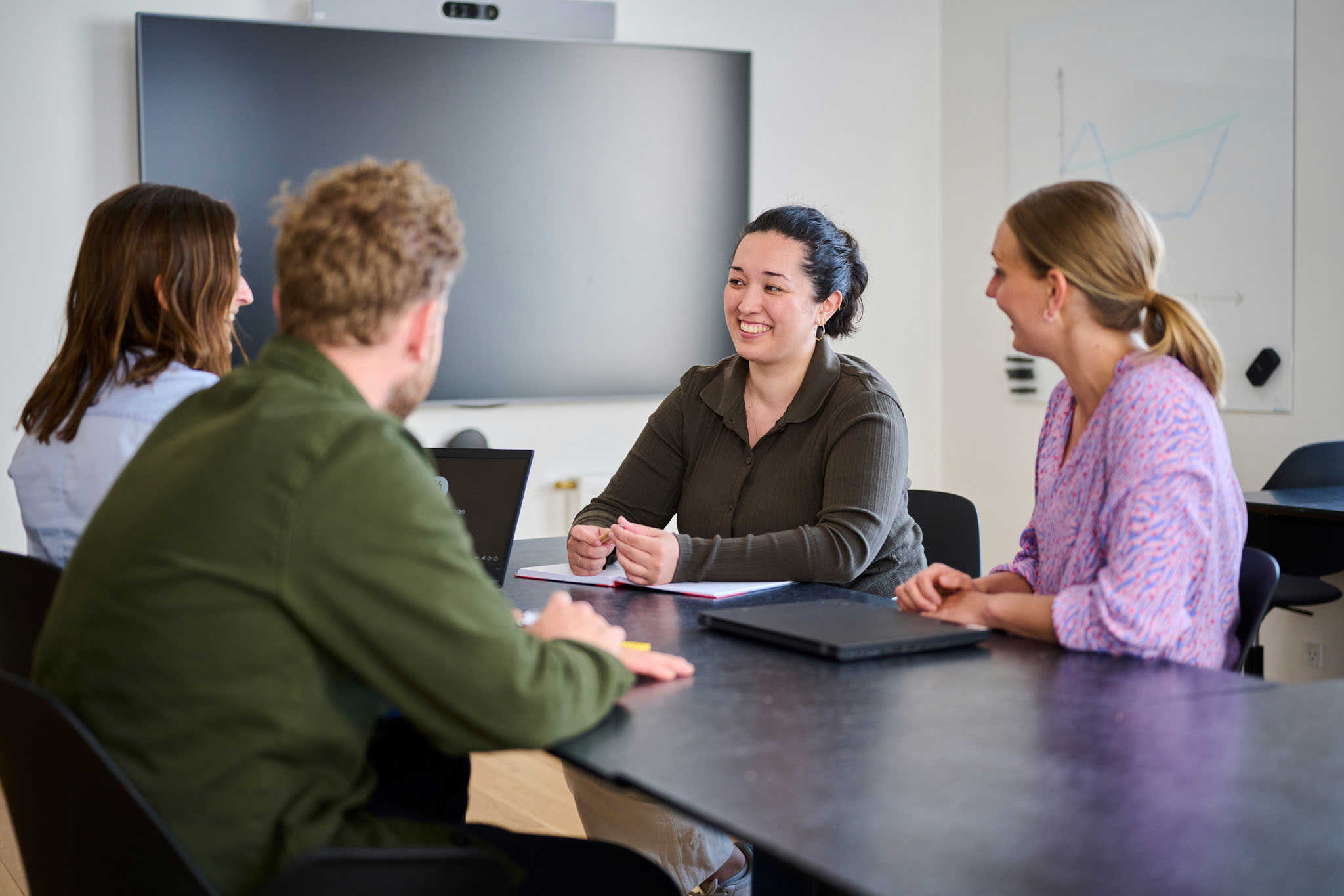Tre kvinder og en mand sidder rundt om bord og snakker