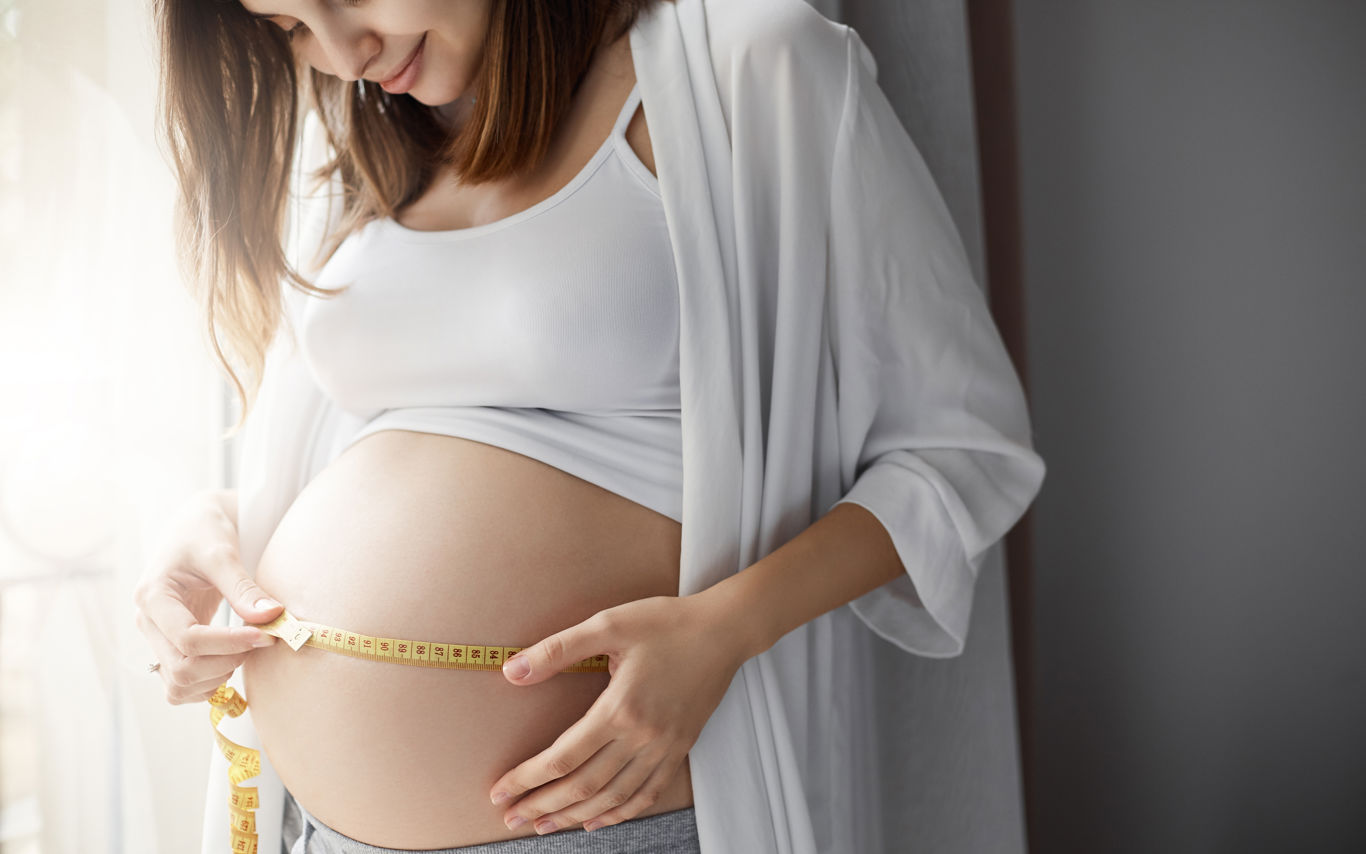 Gravid kvinde måler sin mave med en cemtimetermål