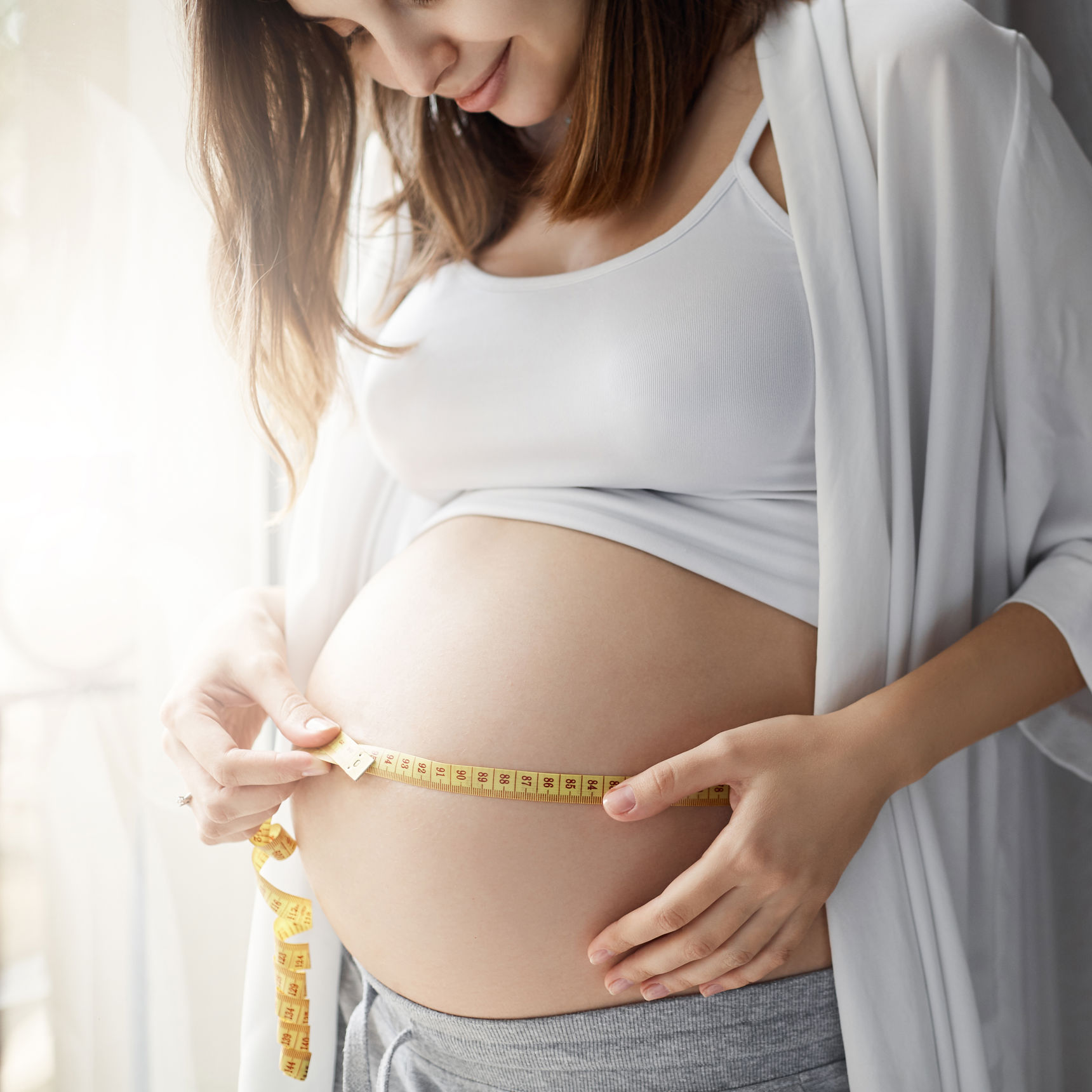 Gravid kvinde måler sin mave med en cemtimetermål