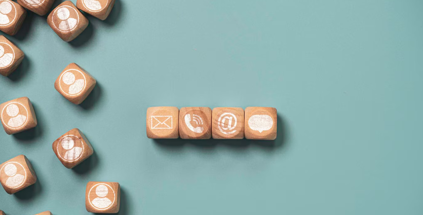 Fire terninger af træ lagt ved siden af hinanden. Terningerne har hvert sit symbol. En med et brev, en med en telefon, en med et @ og den sidste med en taleboble.