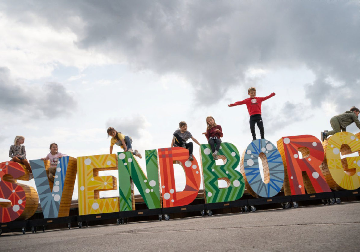 Børn fra indskolingen leger på store farverige bogstaver, hvor der står Svendborg