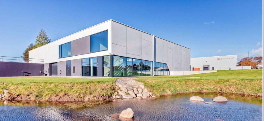 En firkantet bygning med store glaspartier og en lille sø i forgrunden