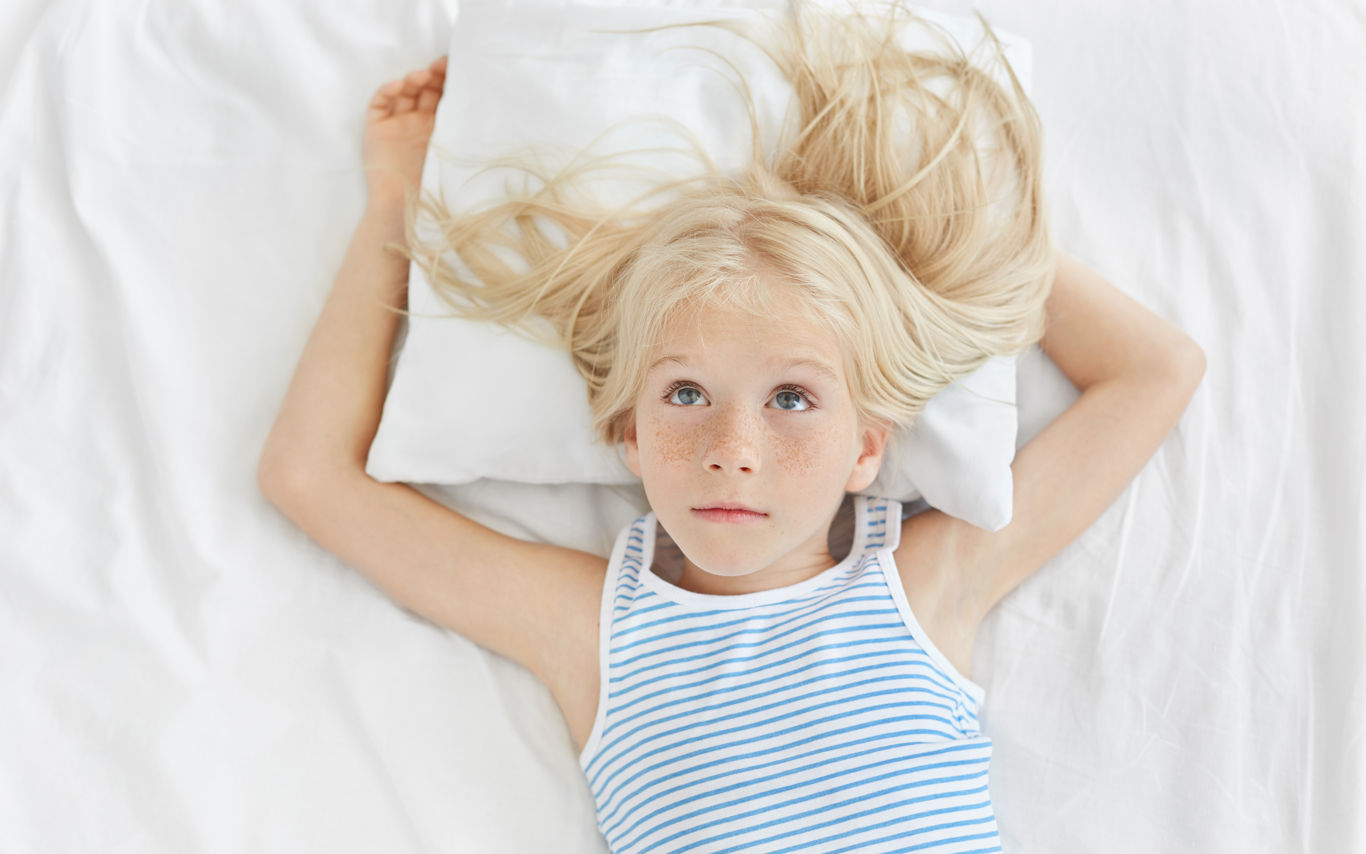 En lyshåret pige ligger i en seng