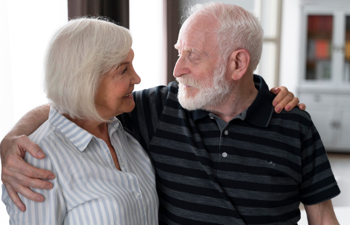 Et ældre par står tæt sammen, smiler og kigger hinanden smilende i øjnene.