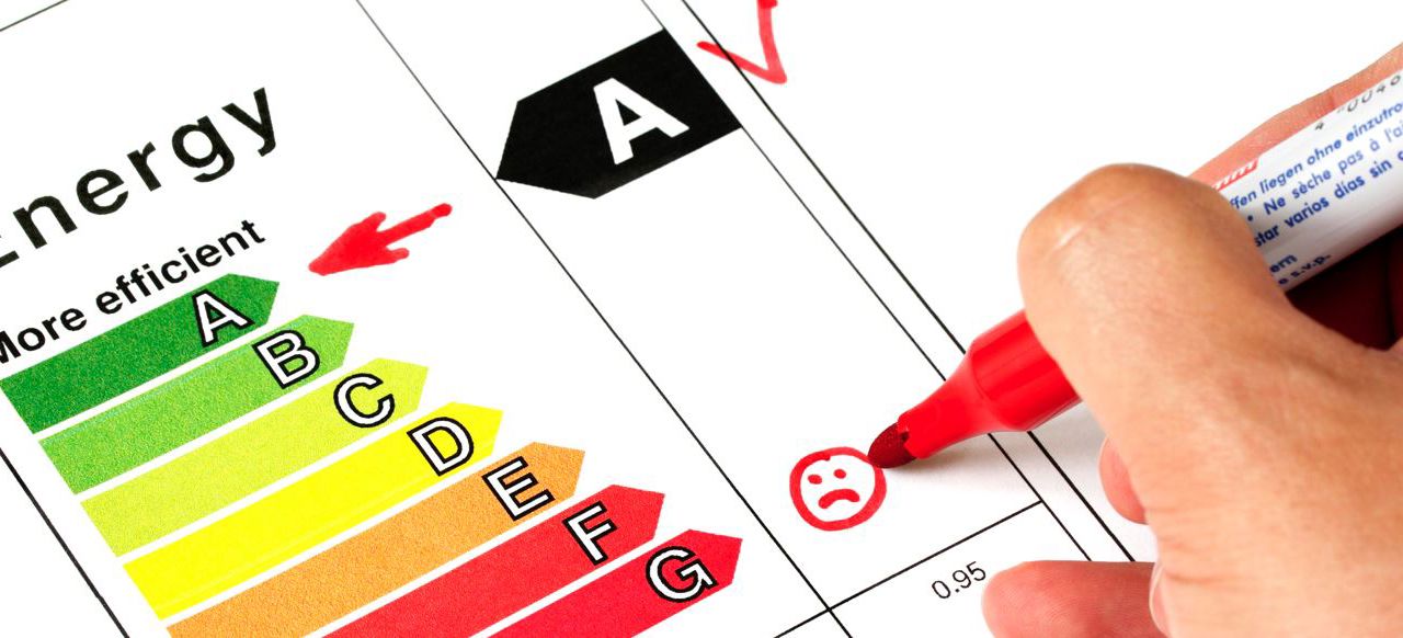 Energimærkeskalaen fra A til G, hvor A er markeret med en pil. Der ses dele af en hånd, som med en rød tusch er ved at notere noget på skalaen