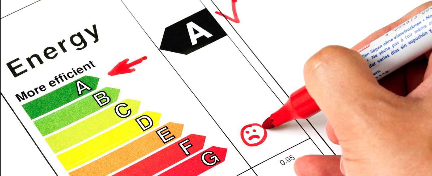 Energimærkeskalaen fra A til G, hvor A er markeret med en pil. Der ses dele af en hånd, som med en rød tusch er ved at notere noget på skalaen