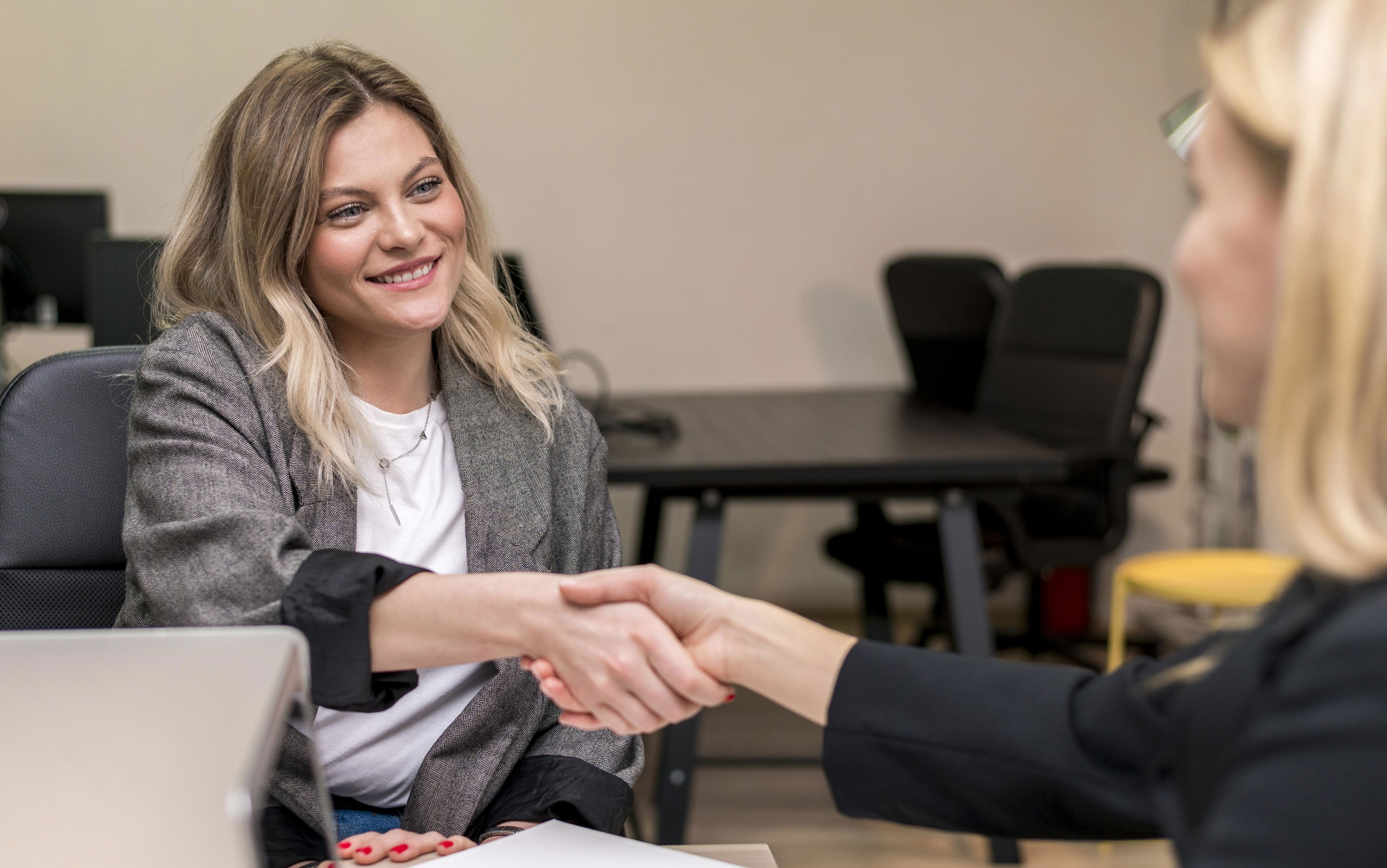 To kvinder trykker hånd. Den ene kvinde har en computer foran sig.