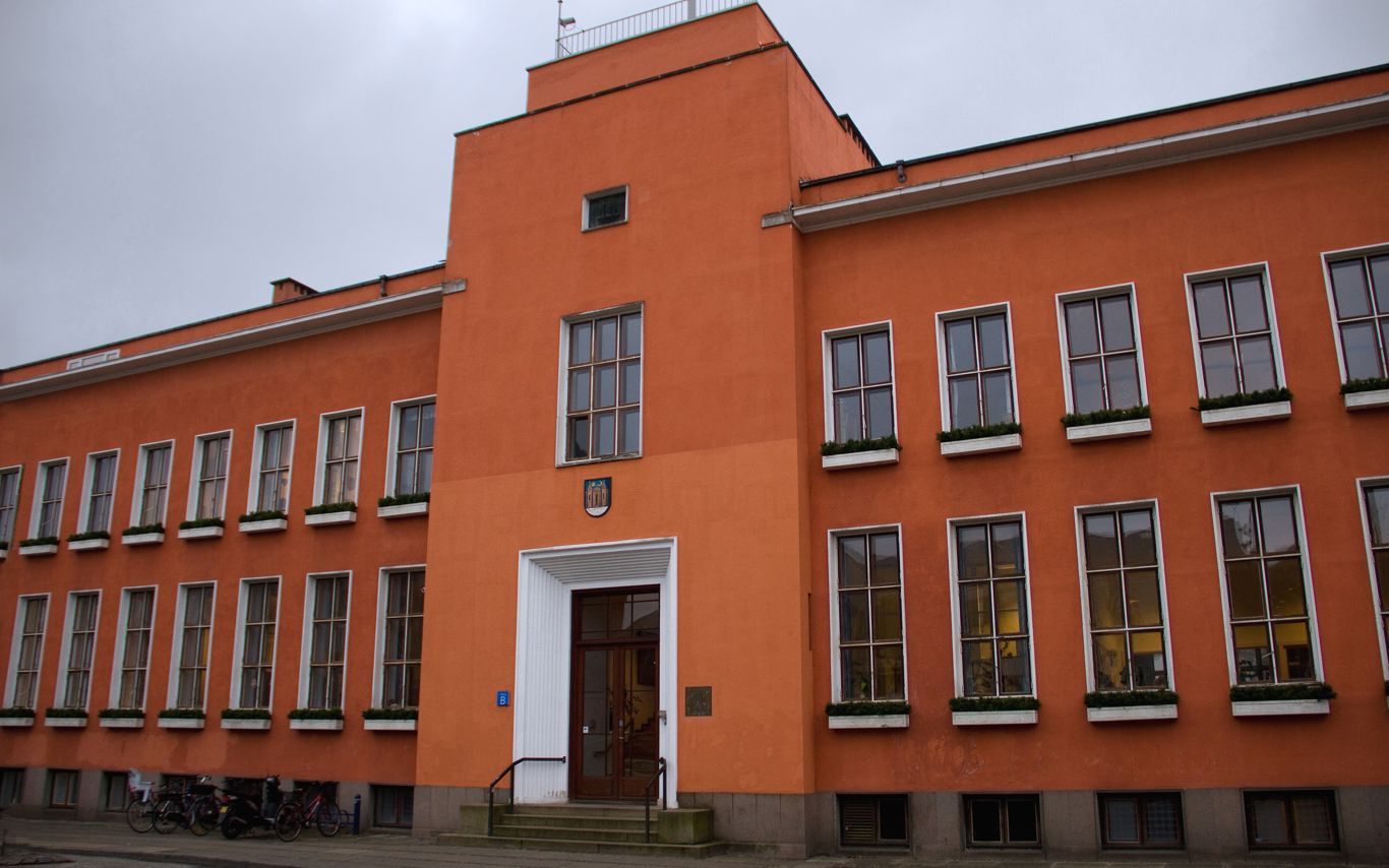 En stor rødlig bygning med brune og hvide vinduesrammer, der viser at bygningen har to etager.