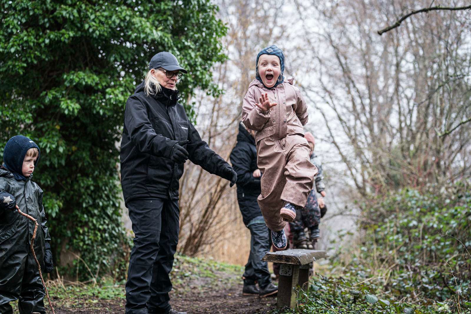 Et barn i Skårup Skovmølle springer fra en bænk, mens en voksen passer på.