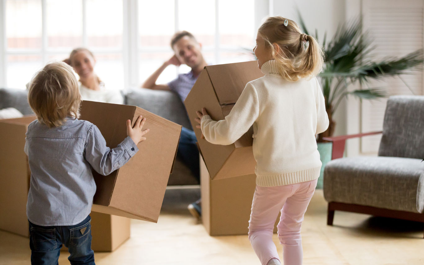 Børn leger med flyttekasser mens forældre sidder i sofa og kigger på