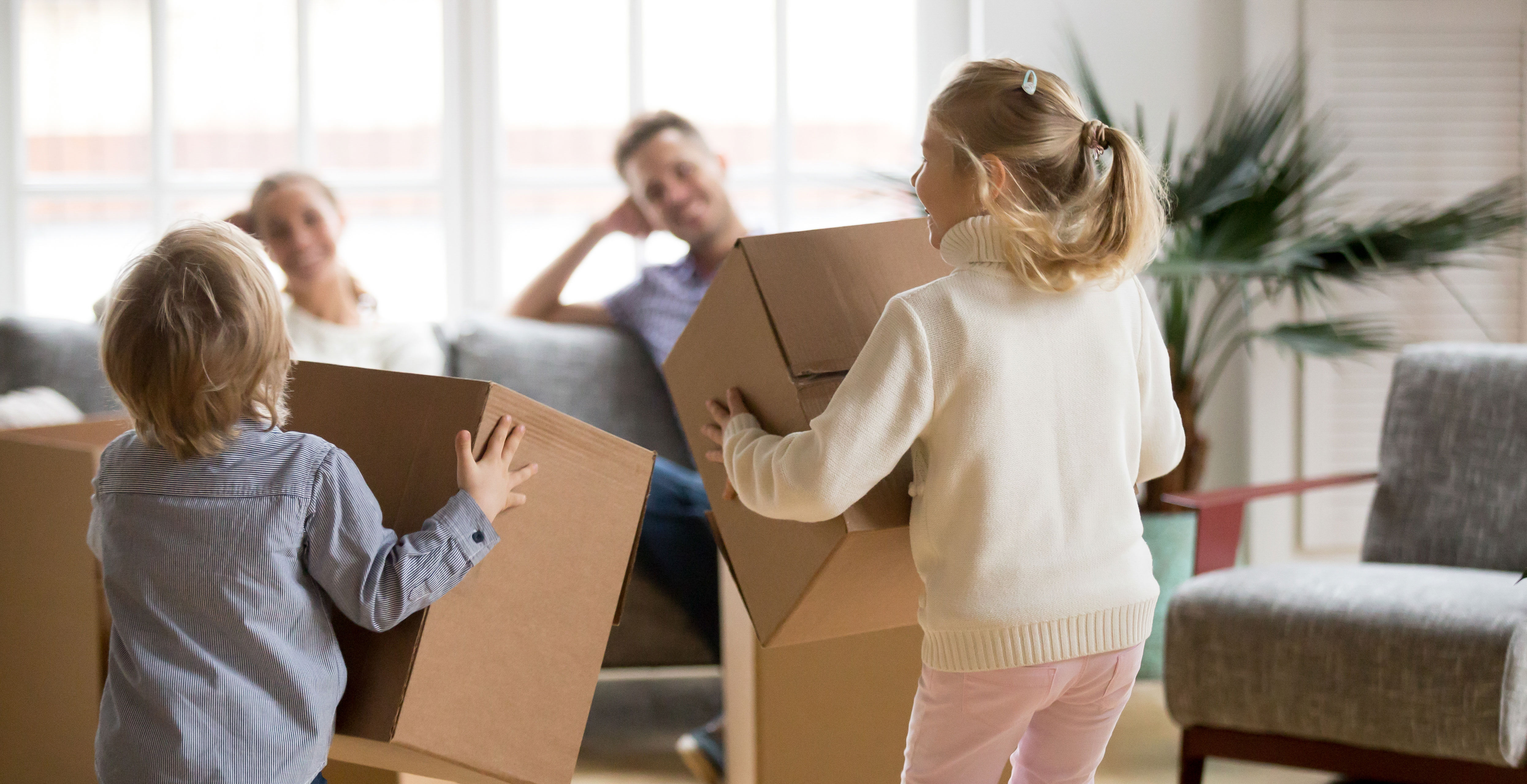 Børn leger med flyttekasser mens forældre sidder i sofa og kigger på