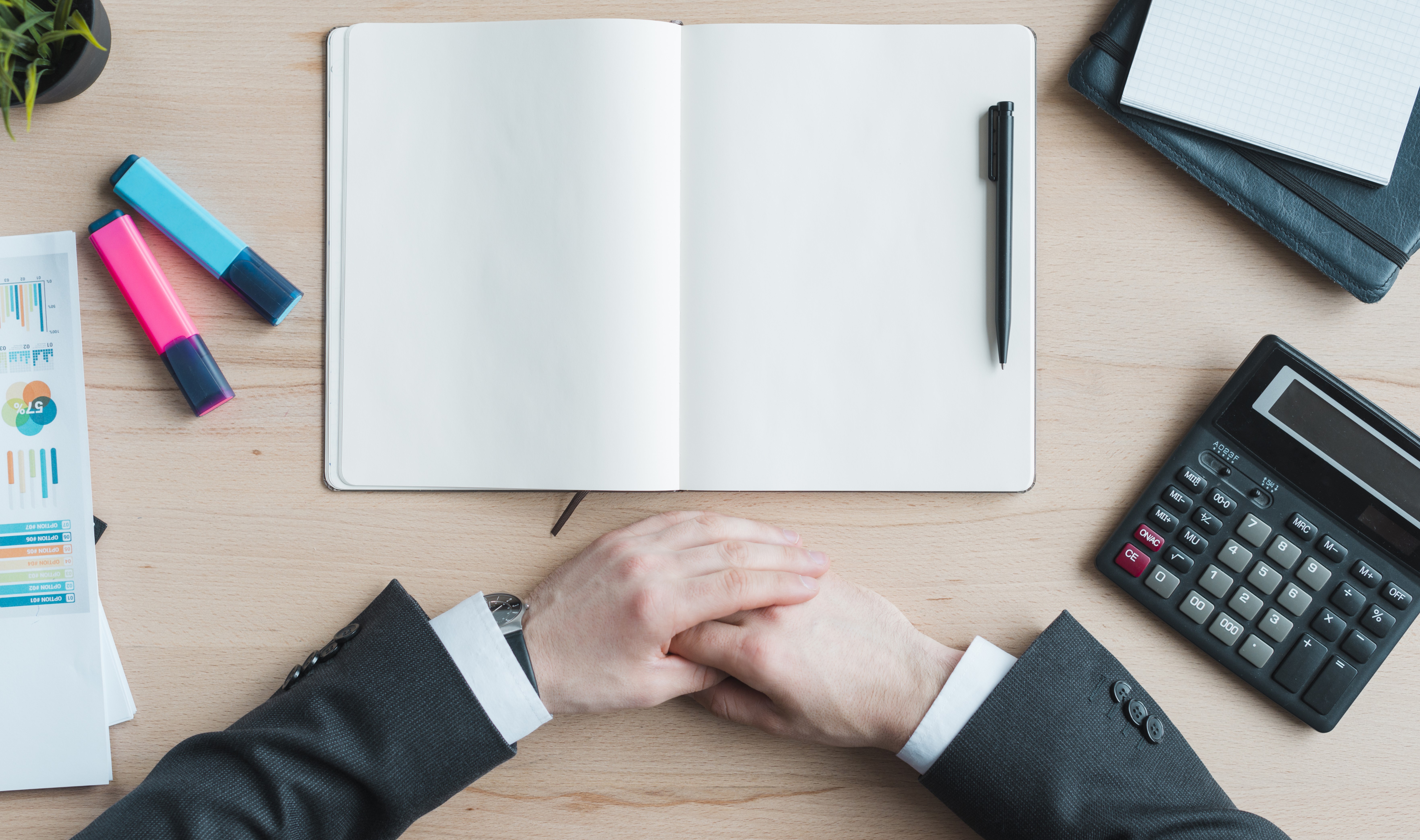 hænder der er foldet sammen. et hæfte, en lommeregner, en kalender. overstregstudser.  en plante