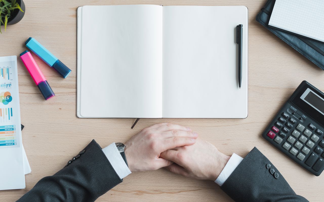hænder der er foldet sammen. et hæfte, en lommeregner, en kalender. overstregstudser. en plante