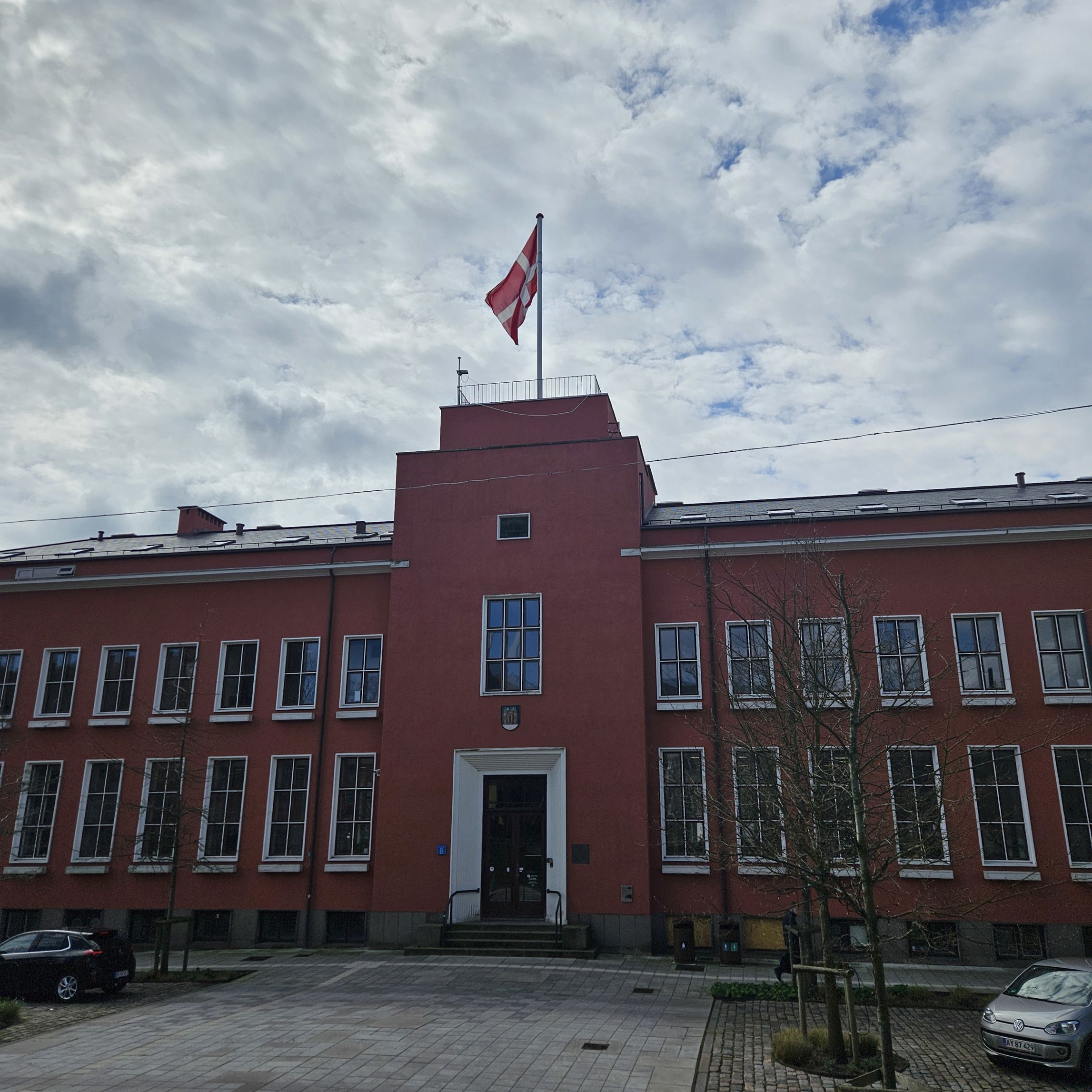 En to-etagers rødlig bygning med hvide vinduesrammer. Øverst på bygningen vejrer Dannebrog. Det er Svendborg Rådhus.