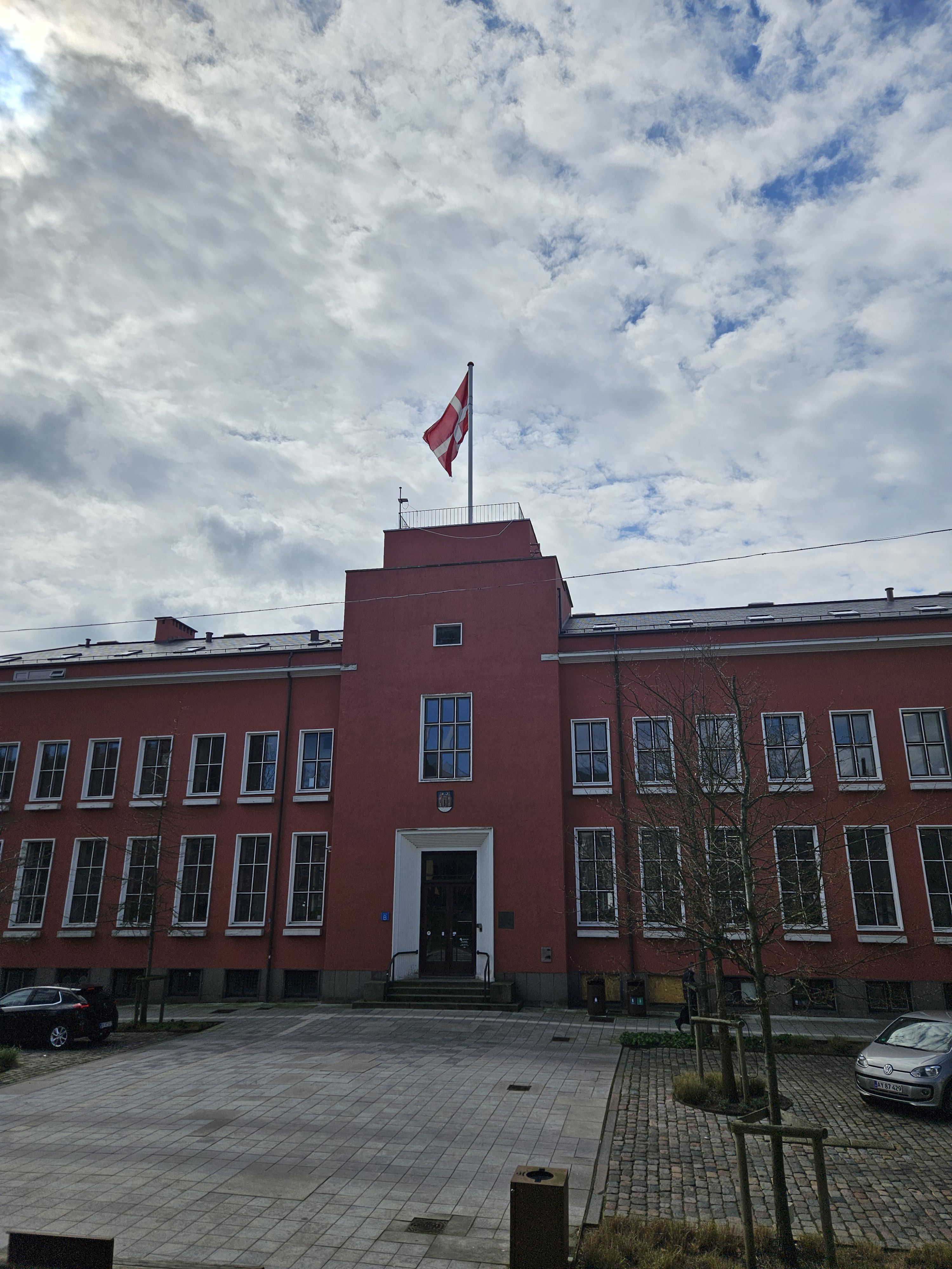 En to-etagers rødlig bygning med hvide vinduesrammer. Øverst på bygningen vejrer Dannebrog. Det er Svendborg Rådhus.